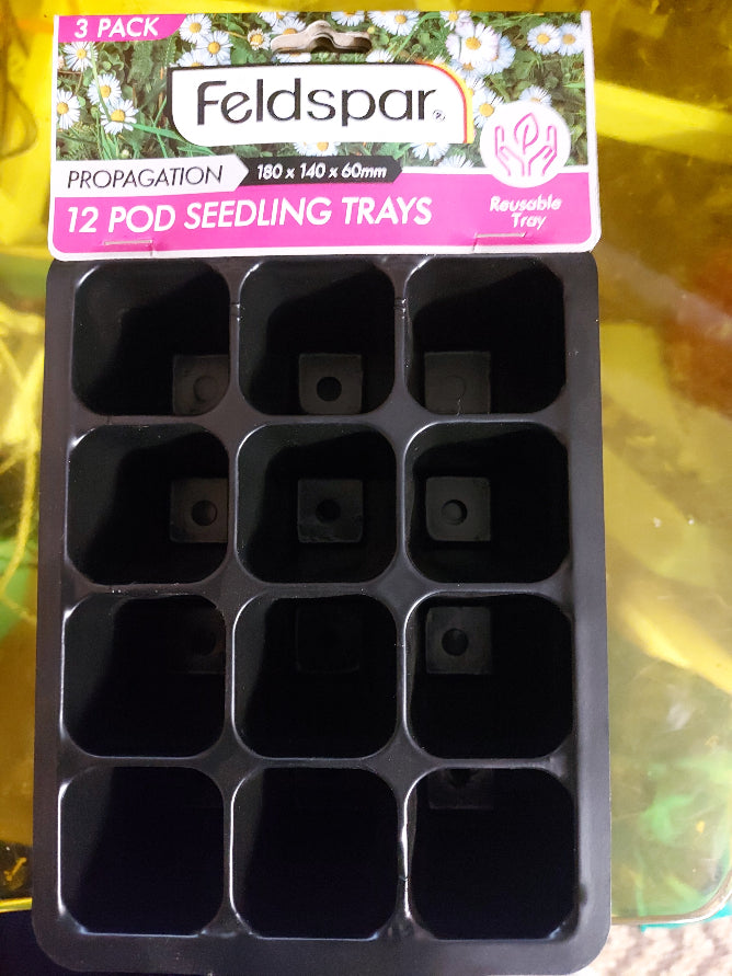 A 12-pod seedling tray in black plastic with a printed header card. The header card is pink and white with daisy graphics and reads 'Feldspar 12 Pod Seedling Trays' and '3 Pack'.